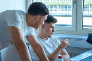 Zwei Lernende sitzen am Tisch vor dem Laptop und arbeiten an ihrem Start-up-Pitch.